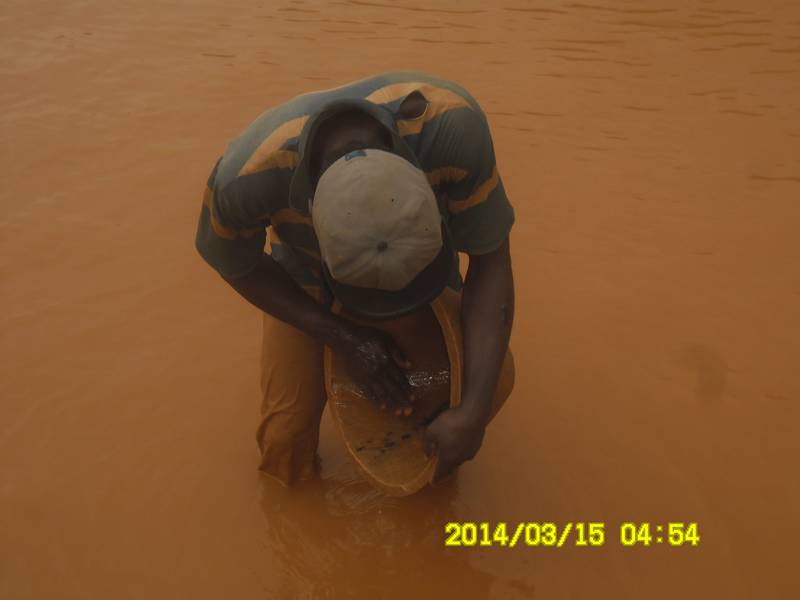 Miner panning for gold with traditional wooden bowl in Ghana